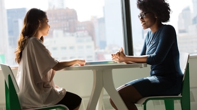 two women sitting beside table and talking