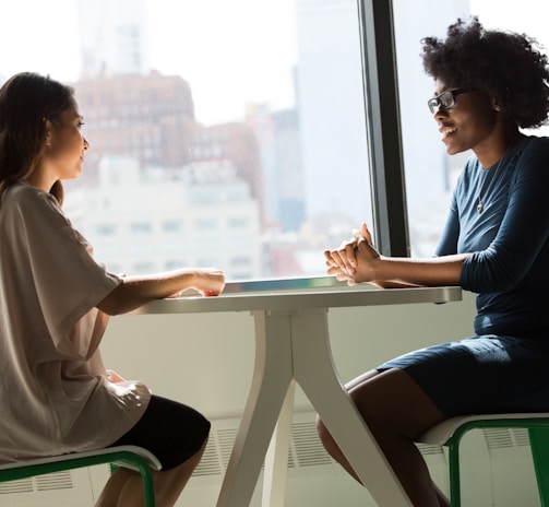 two women sitting beside table and talking