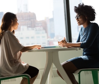 two women sitting beside table and talking