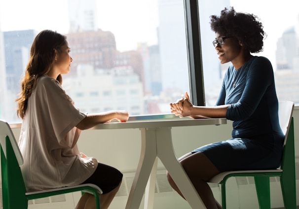 two women sitting beside table and talking