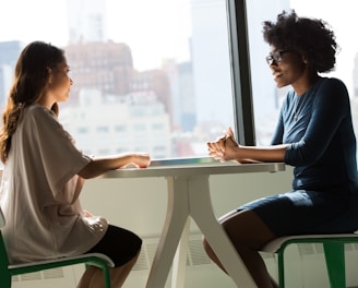 two women sitting beside table and talking