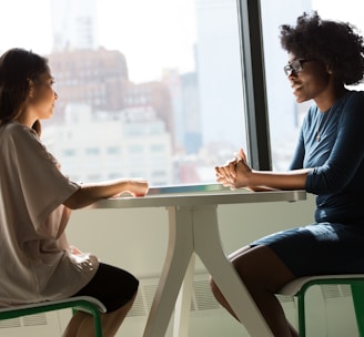 two women sitting beside table and talking