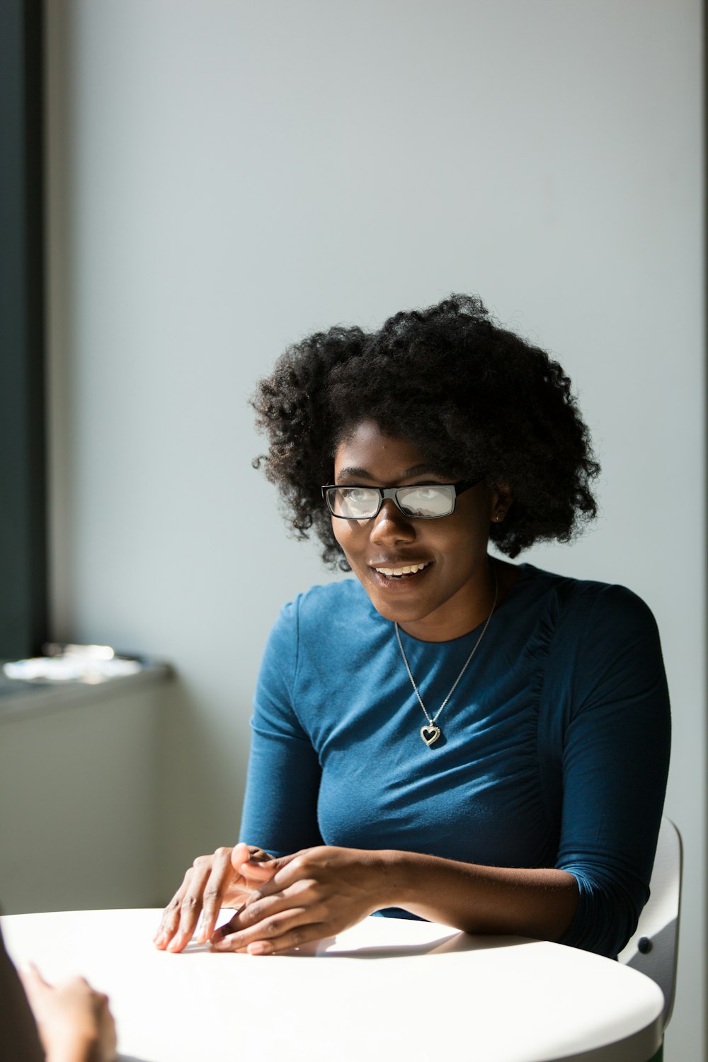 smiling woman wearing blue shirt sitting beside table