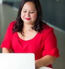 smirking woman wearing red top using laptop computer