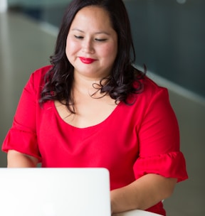 smirking woman wearing red top using laptop computer