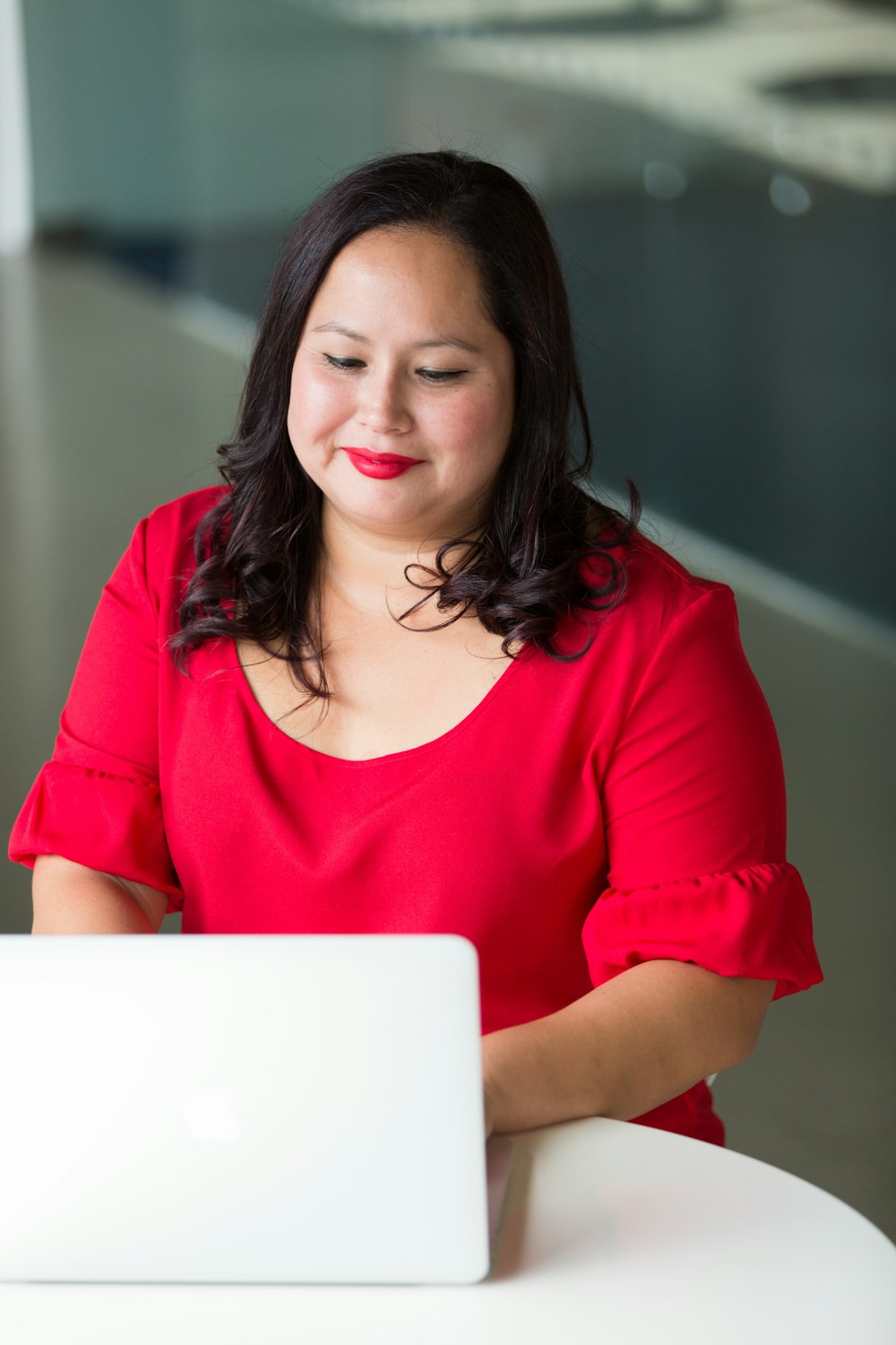 smirking woman wearing red top using laptop computer