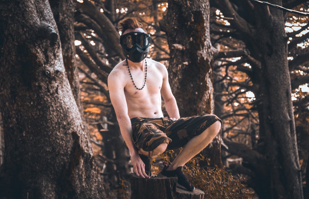 man squatting and wearing paintball mask near trees