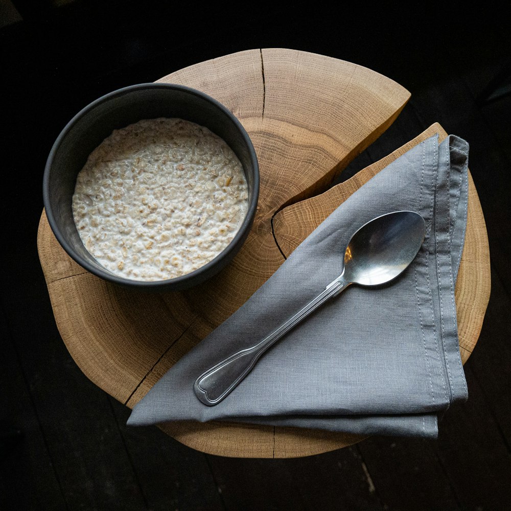 bowl of cereal beside spoon on wood slab
