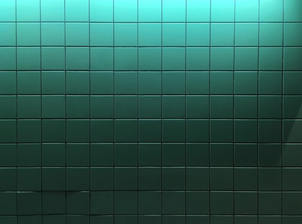 A wall covered in square tiles that are predominantly green, with a gradient effect as the color transitions from a lighter shade at the top to a darker shade at the bottom.