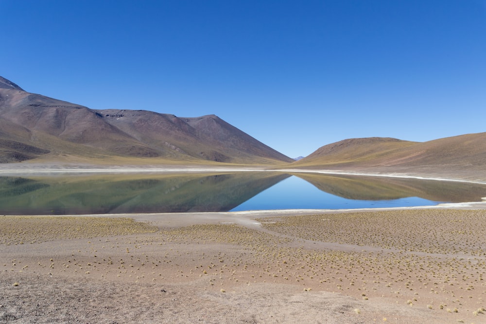 body of water near mountain under blue sky