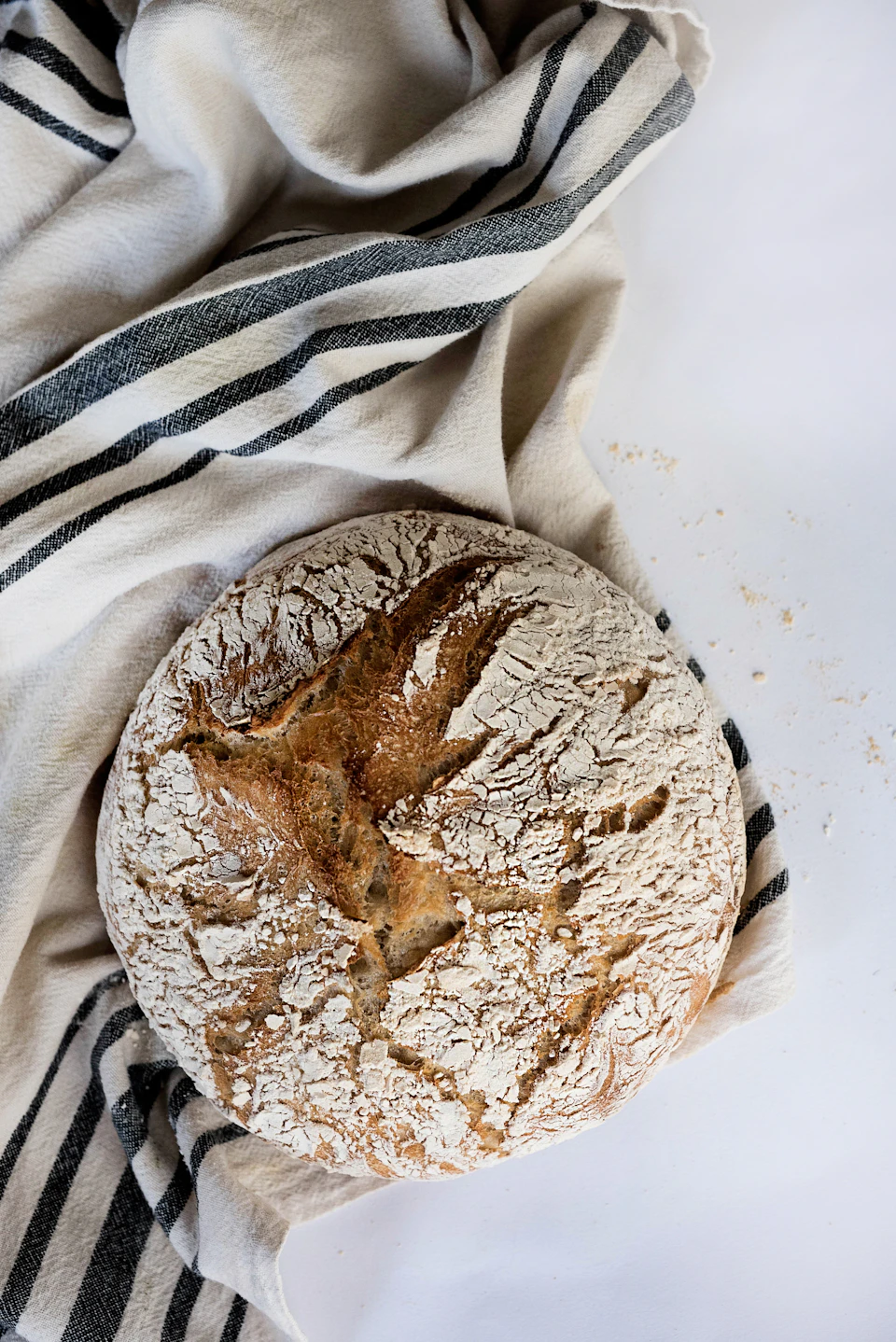 Round loaf of bread rests on white cloth with black stripes, slightly tilted to left