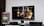 A flat-screen TV displays a video game interface featuring a character from Mortal Kombat in the center. Beside the TV is a stack of video game cases for the PlayStation 3, including titles like FIFA 14 and Grand Theft Auto. Below the TV, there is a gaming console, controllers, and other gaming equipment.