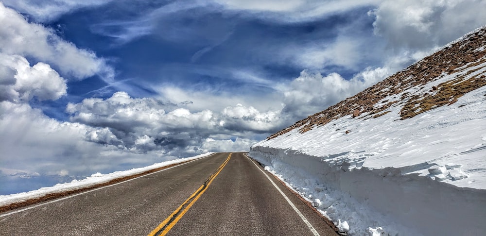 panoramic view of highway near snow covered hills during cloudy day
