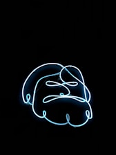 A neon light in the shape of a stylized angry face against a black background. The lines form expressive features like furrowed brows and a downturned mouth.