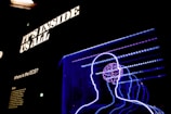 Bright neon outlines of human figures superimposed with a detailed sketch of a brain against a dark background. Above the figures, bold, illuminated text reads 'IT'S INSIDE US ALL'. There is also a small text panel on the left side with the title 'Where is the ECS?' and some descriptive text underneath.