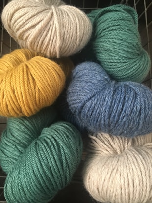 A collection of yarn skeins in various colors including light gray, green, blue, and yellow. They are neatly arranged in a basket.