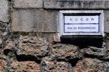 A street sign with the words 'Rua da Ressurreição' is mounted on a textured stone wall. The sign has both Chinese and Portuguese text, with a blue and white color scheme.
