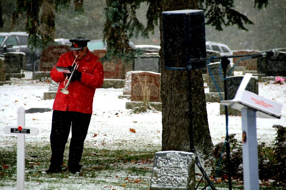 man wearing red jacket blowing trumpet near cemetery