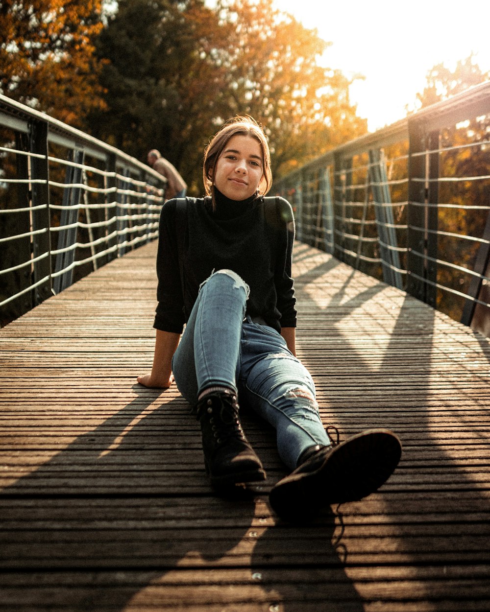 woman in black high-neck sweater and blue jeans sitting on woodn bridge