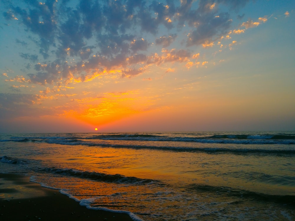 a sunset over the ocean with waves coming in