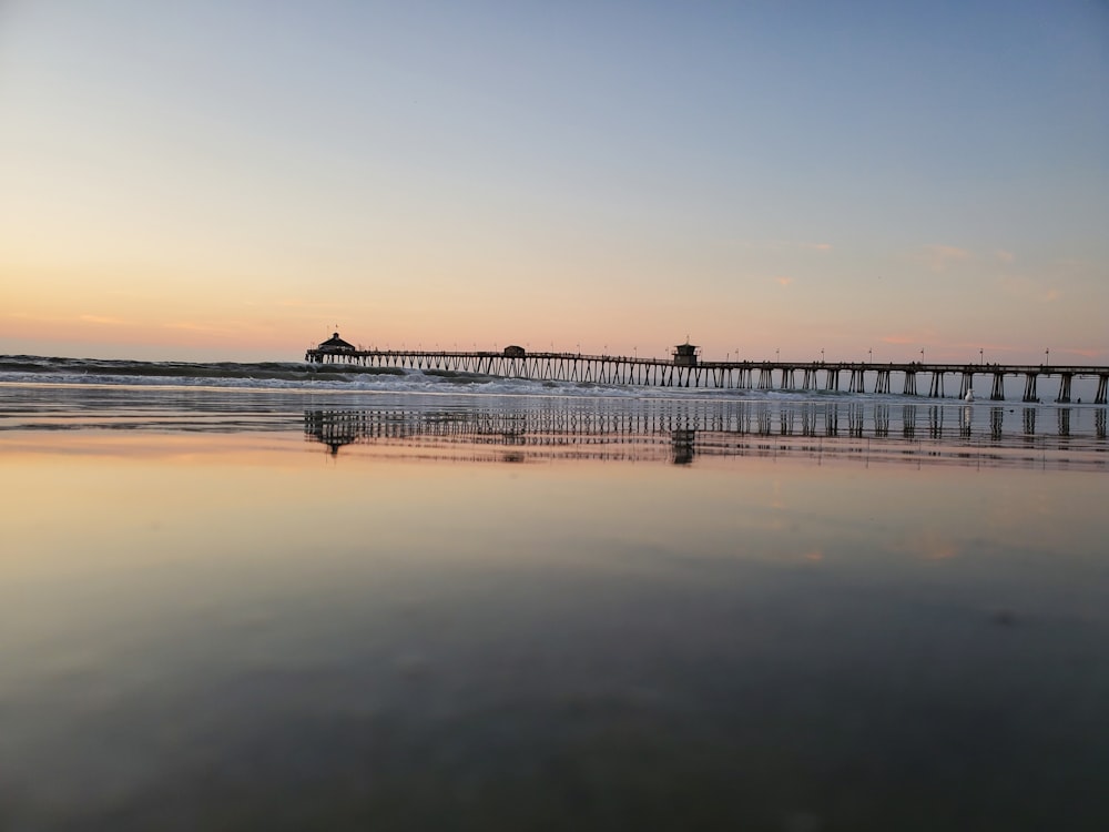 black steel bridge viewing body of water under blue and orange sky