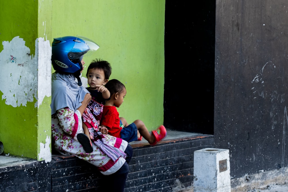 woman wearing helmet sitting while carrying baby and another child sitting