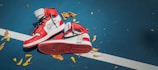 A pair of red and white sneakers lie on a blue court with scattered yellow and brown leaves. The sneakers feature prominent branding and text details.