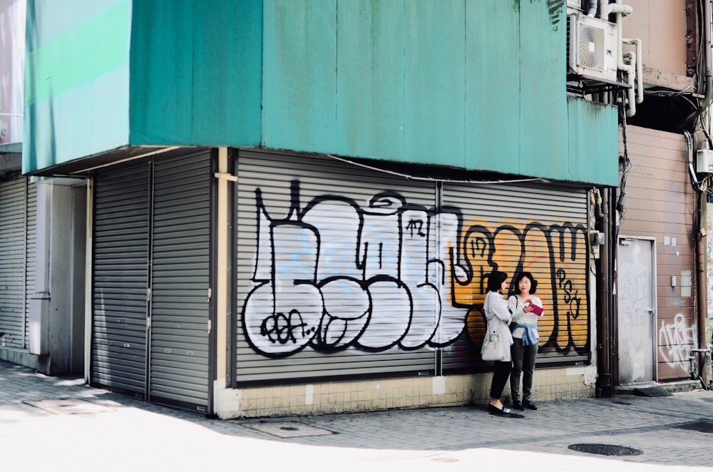 two woman standing near graffiti