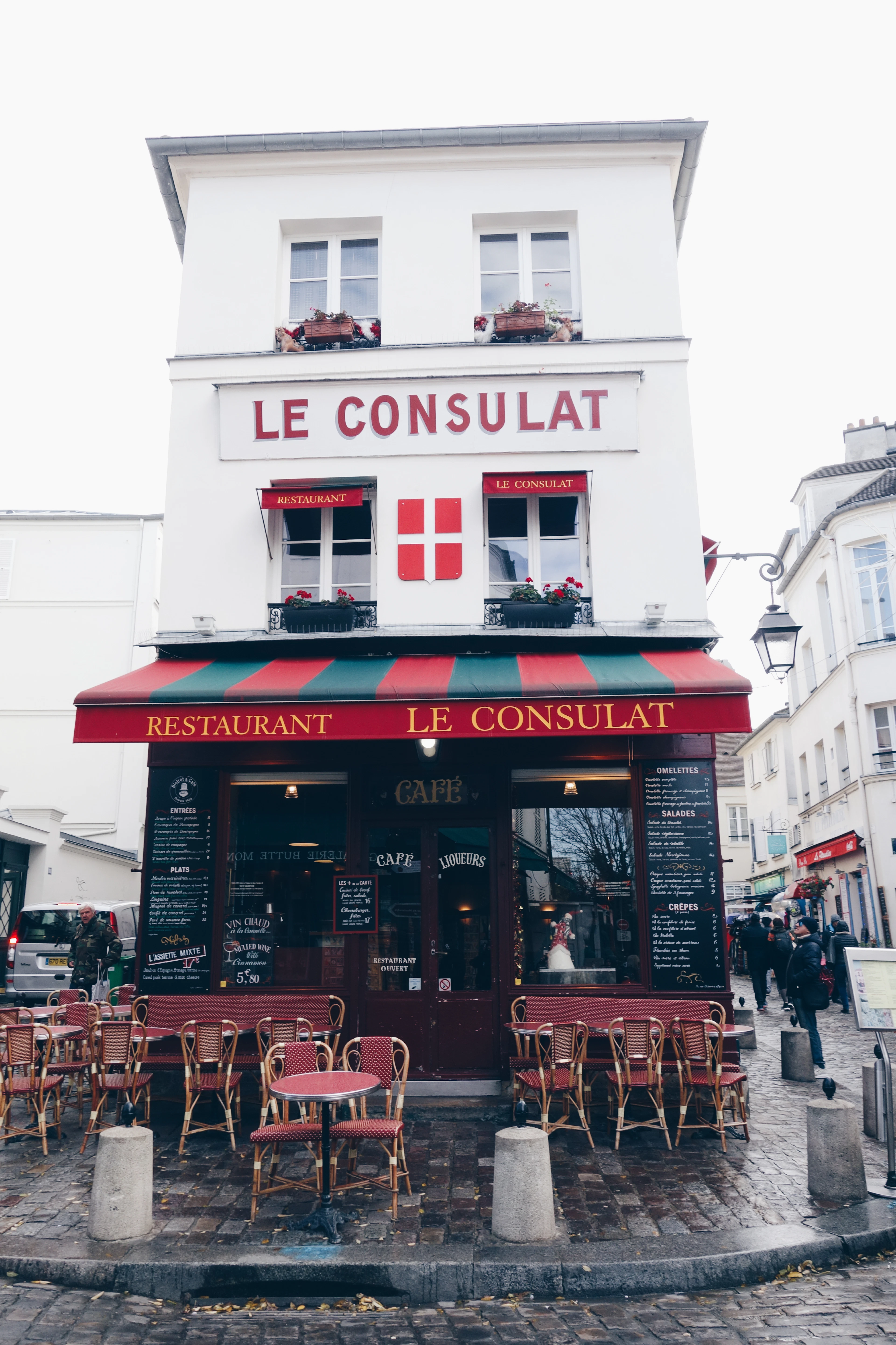 The red and green awning and cane terrace chairs of the Le Consulat cafe on a cobbled Montmartre corner, Paris