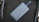 A sleek, matte-finished power bank with the number 5100 on it lies on a textured dark material. A blue strap is attached to the power bank.