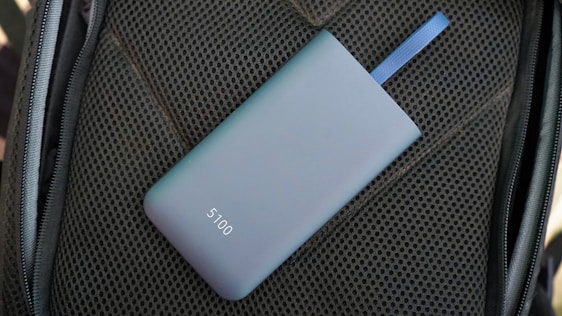 A sleek, matte-finished power bank with the number 5100 on it lies on a textured dark material. A blue strap is attached to the power bank.