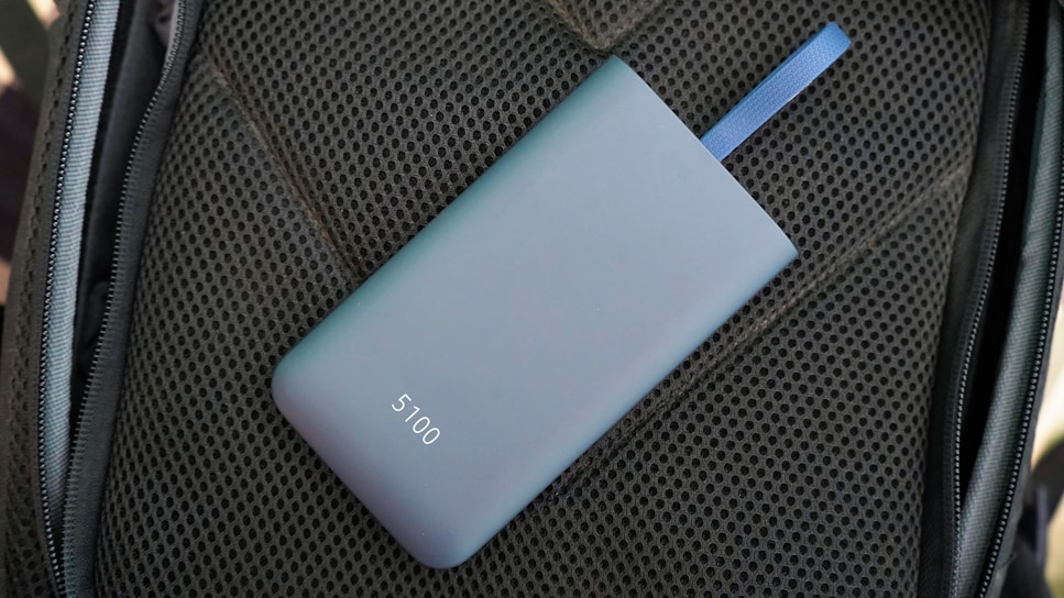 A sleek, matte-finished power bank with the number 5100 on it lies on a textured dark material. A blue strap is attached to the power bank.