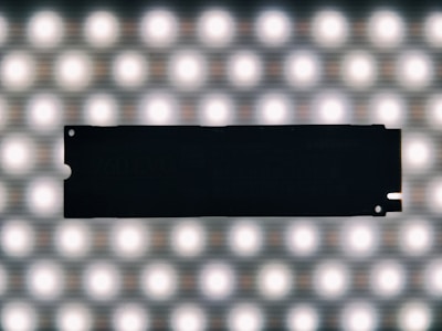 A silhouette of a solid-state drive against a bright grid of evenly spaced circular lights, creating a contrasting effect.