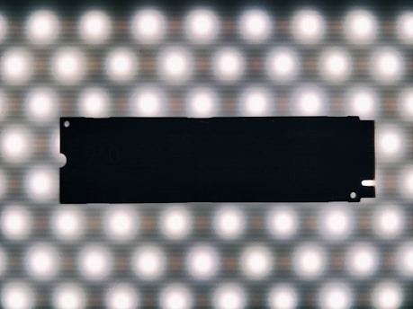 A silhouette of a solid-state drive against a bright grid of evenly spaced circular lights, creating a contrasting effect.