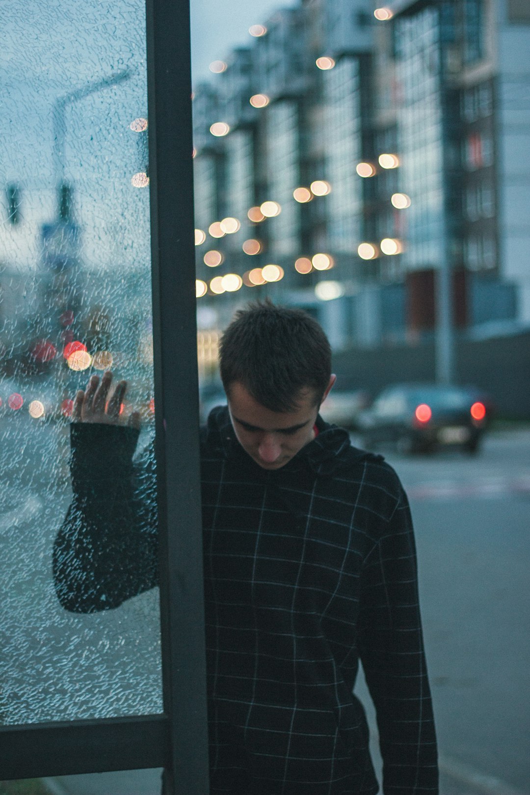 man in black and gray plaid hoodie jacket leaning in glass window