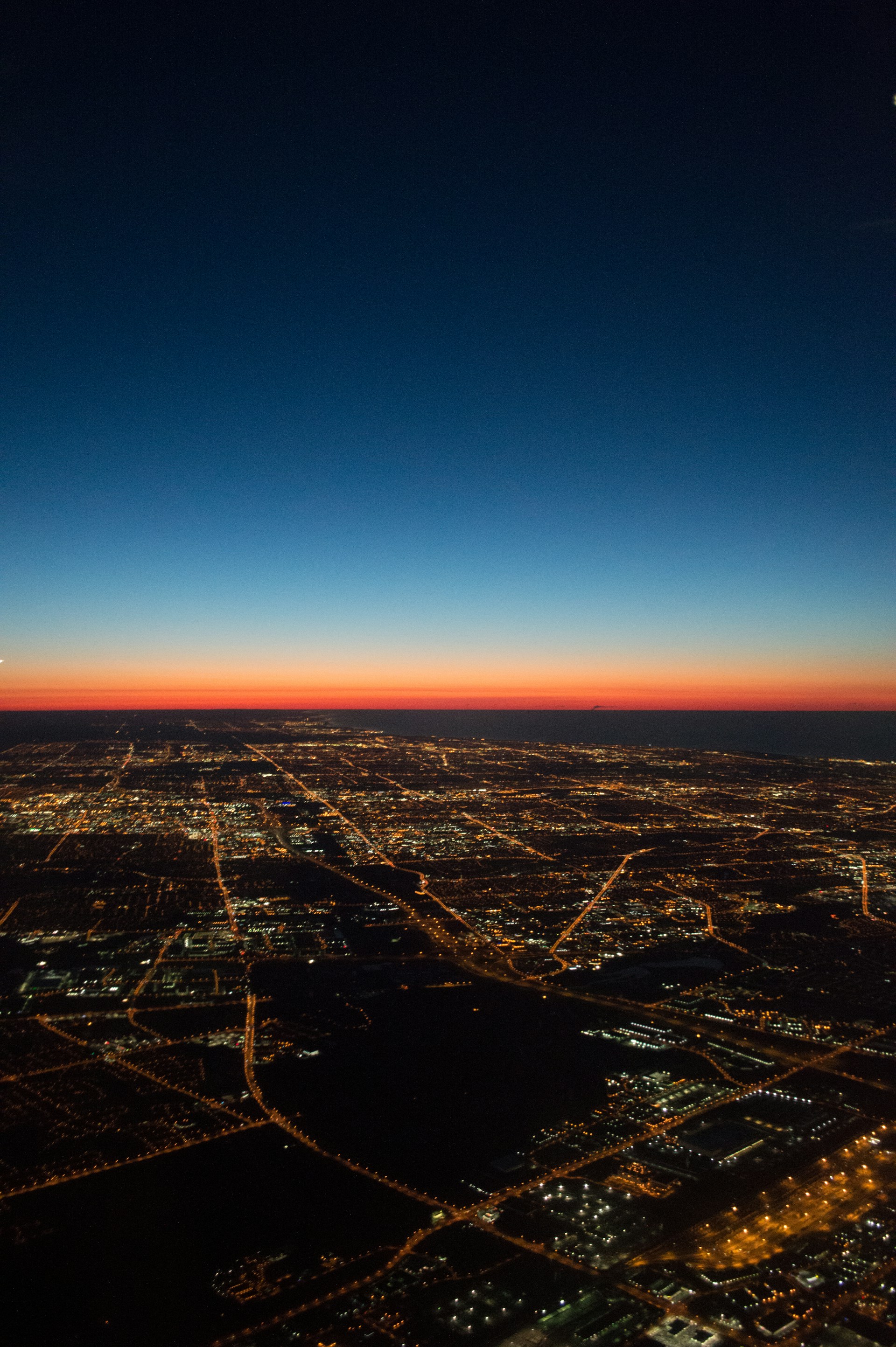 An aerial shot captured by a drone showing a futuristic cityscape at dusk, with glowing lights and smooth gradients of black, white, and red.