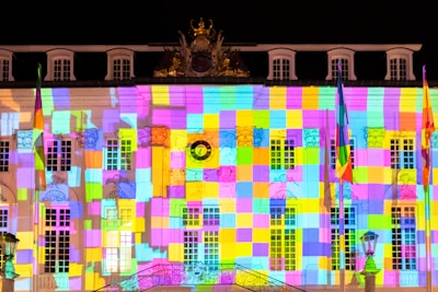 Close-up of intricate projection mapping illuminating a complex geometric architectural façade in neon hues.