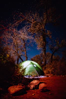 Close-up of a sturdy camping tent pitched on rocky terrain under a starry night sky.