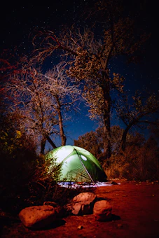 Close-up of a sturdy camping tent pitched on rocky terrain under a starry night sky.