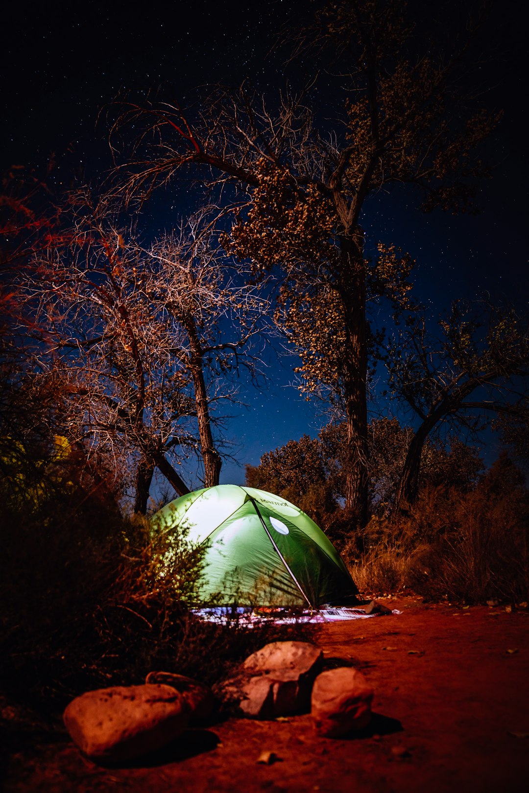 green camping tent near trees and rocks