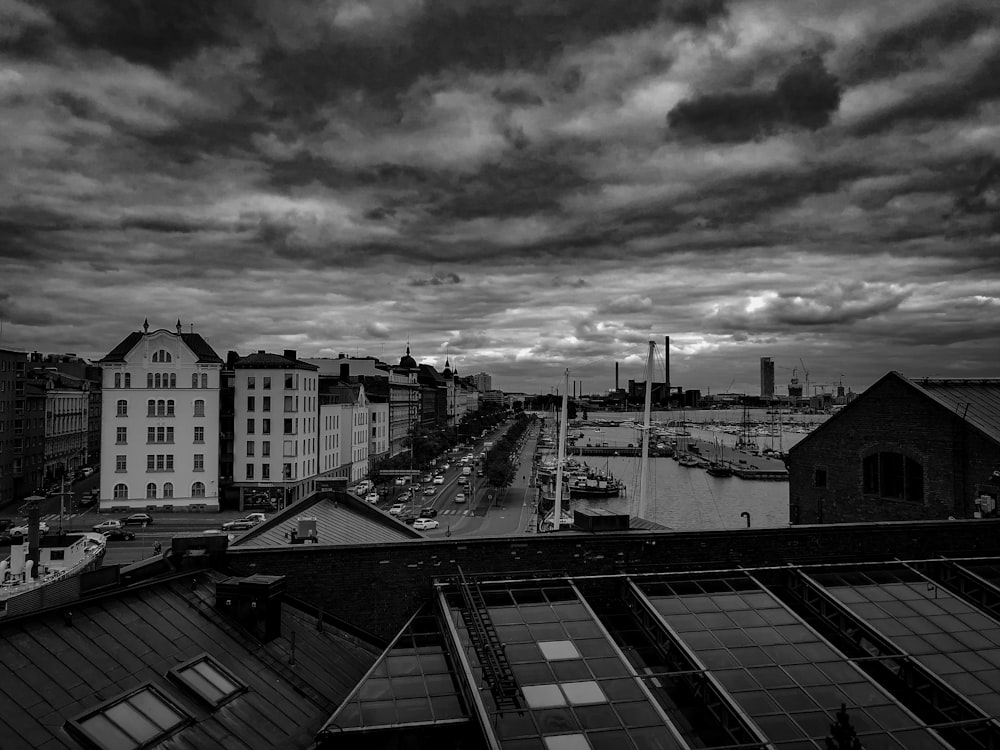 grayscale photo of buildings near body of water under cloudy sky