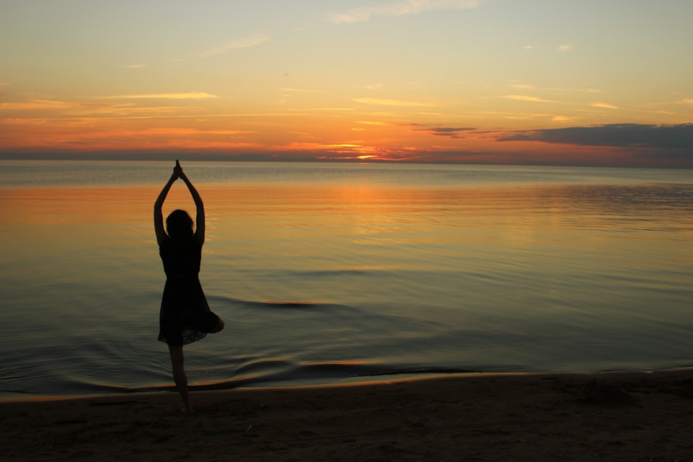 Mujer haciendo yoga cerca de un cuerpo de agua tranquilo durante la hora dorada