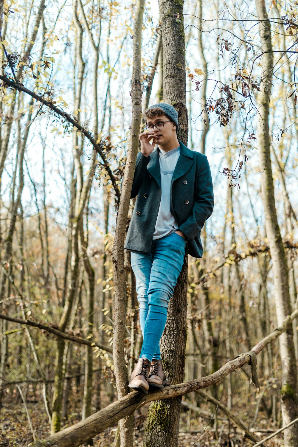 woman in black coat and blue jeans standing on wood log beside tree