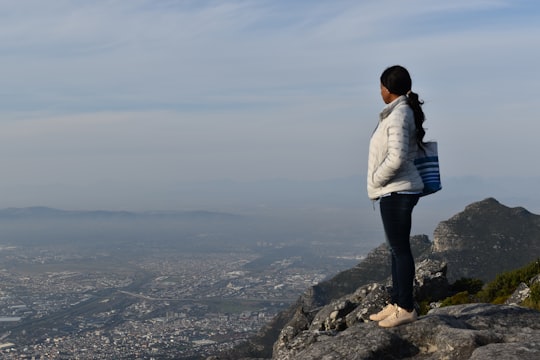 woman in white puffer jacket standing on rocky cliff in Table Mountain South Africa