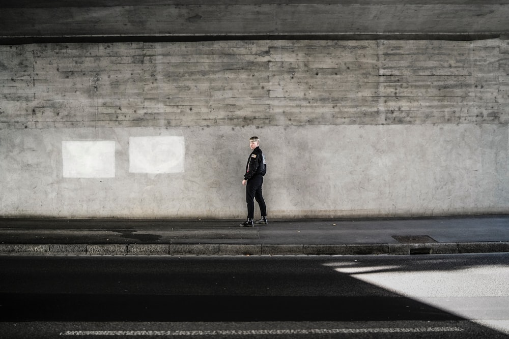 person in black attire by concrete wall