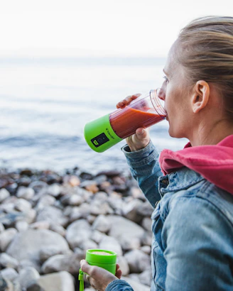 woman drinking green from single-serve blender facing boulders