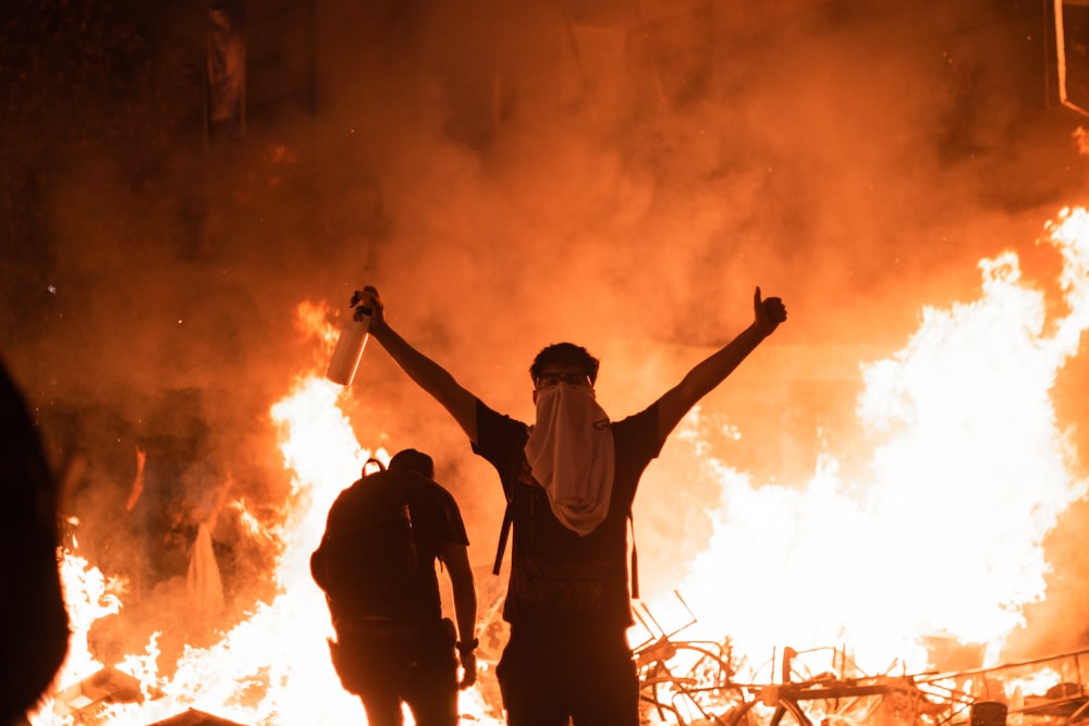 a man standing in front of a fire with his arms in the air