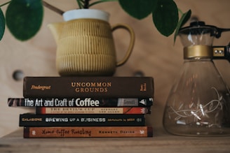 A rustic wooden table displaying a stack of well-loved coffee brewing and lifestyle books