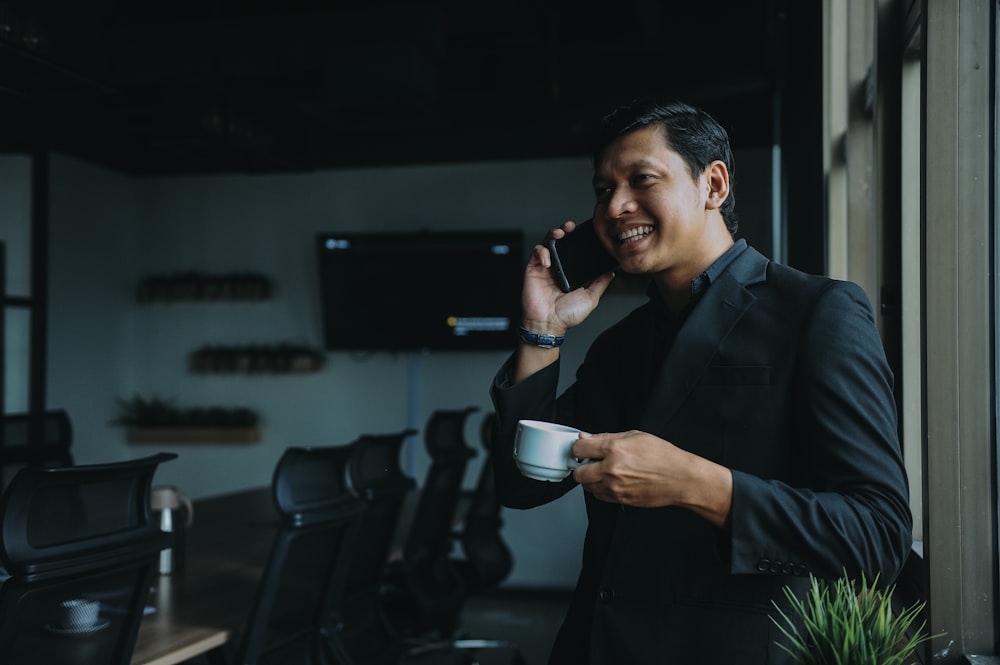 Hombre sonriente sosteniendo la taza y usando el teléfono inteligente