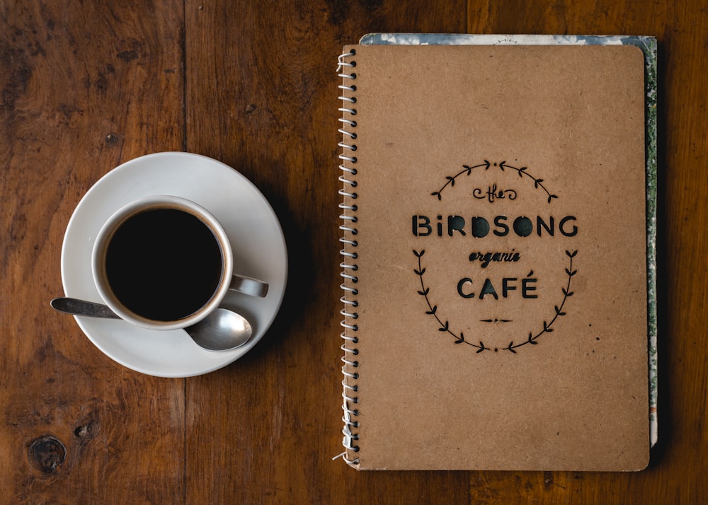 white coffee mug on saucer beside notebook